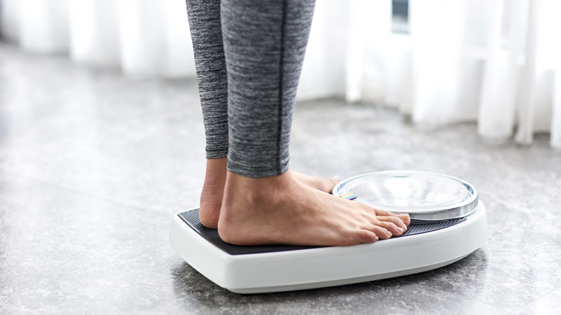 Plano de pormenor com pernas e pés de mulher com calças fitness, a pesar-se numa balança